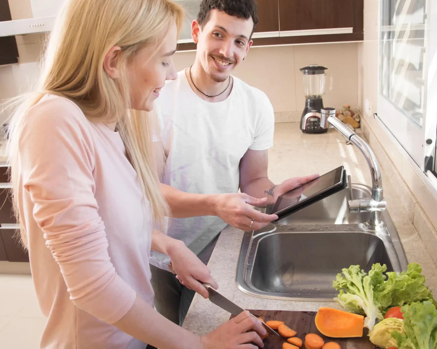 woman-cutting-carrot-chopping-board-looking-digital-tablet-hold-by-his-friend